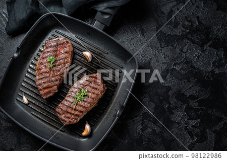 Grilled Top Blade or flat iron roast beef meat steaks on a skillet. Black background. Top View. Copy space 98122986