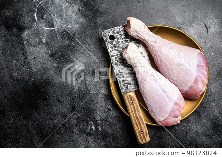 Fresh turkey legs Drumsticks, raw Poultry meat with butcher cleaver. Black background. Top view. Copy space 98123024