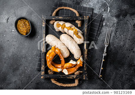 Bavarian meal with white sausages and sweet mustard in wooden tray with Pretzel. Black background. Top view Bavarian meal with white sausages and sweet mustard in wooden tray with Pretzel. Black background. Top view 98123169