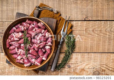 Raw chicken hearts in a wooden plate with herbs. Organic offals. Wooden background. Top view. Copy space 98123201