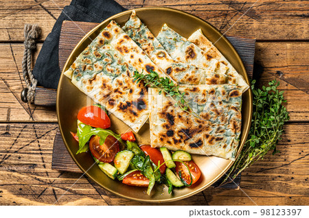 Gozleme flatbread with greens and vegetable salad on garnish. Wooden background. Top view 98123397