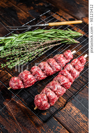 Raw kofta, kofte kebab Skewers with beef and lamb meat and spices ready for cooking. Wooden background. Top view Raw kofta, kofte kebab Skewers with beef and lamb meat and spices ready for cooking. Wooden background. Top view 98123412