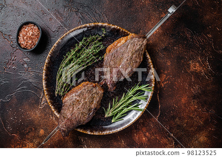 Brazilian BBQ - grilled dry aged picanha beef steak with herbs. Dark background. Top view Brazilian BBQ - grilled dry aged picanha beef steak with herbs. Dark background. Top view 98123525