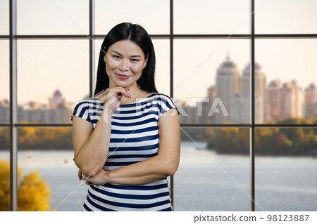 Portrait of a young sexy asian casual-dressed woman posing indoors. River and city view from checkered windows. 98123887