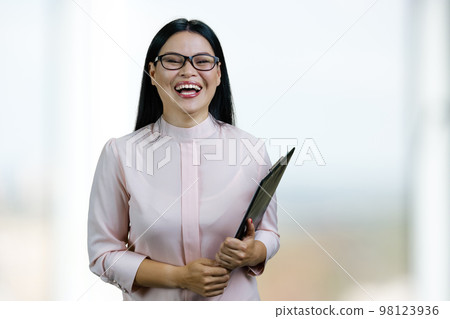 Portrait of a young laughing smart businesswoman with clipboard. Blurred windows background. 98123936