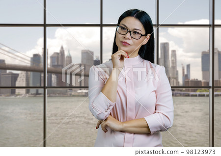 Portrait of pensive young smart asian businesswoman indoors. Chechered windows with cityscape background. Portrait of pensive young smart asian businesswoman indoors. Chechered windows with cityscape background. 98123973