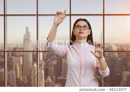 Portrait of young asian woman is interacting with invisible virtual. Checkered windows with cityscape background. 98123977