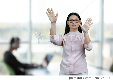 Young asian woman is zooming in objects on imaginary virtual screen for copy space. Office enviroment background. 98123997