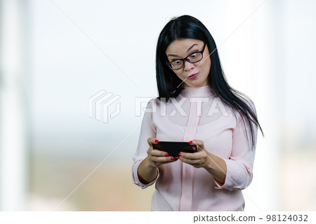 Asian businesswoman is watching something on her smartphone with eyes wide open. Abstract blurred background. Asian businesswoman is watching something on her smartphone with eyes wide open. Abstract blurred background. 98124032