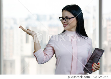 Portrait of a young asian businesswoman holding tablet pc and showing copy space. Blurred indoor windows background. Portrait of a young asian businesswoman holding tablet pc and showing copy space. Blurred indoor windows background. 98124056