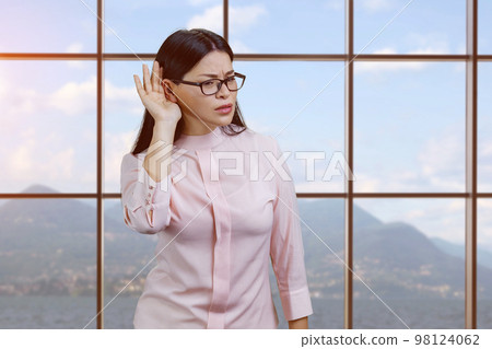 Young asian businesswoman struggles hard to hear you. Checkered window and landscape background. Young asian businesswoman struggles hard to hear you. Checkered window and landscape background. 98124062