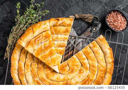 Turkish Tepsi Boregi, Round Borek cheese pie on kitchen board. Black background. Top view Turkish Tepsi Boregi, Round Borek cheese pie on kitchen board. Black background. Top view 98125435