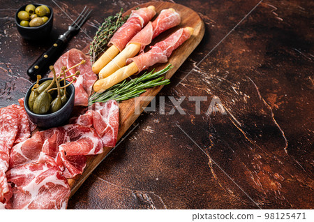 Meat appetizer platter with grissini sticks, Prosciutto crudo, Salami and Coppa Sausage and olives. Dark background. Top view. Copy space Meat appetizer platter with grissini sticks, Prosciutto crudo, Salami and Coppa Sausage and olives. Dark background. Top view. Copy space 98125471