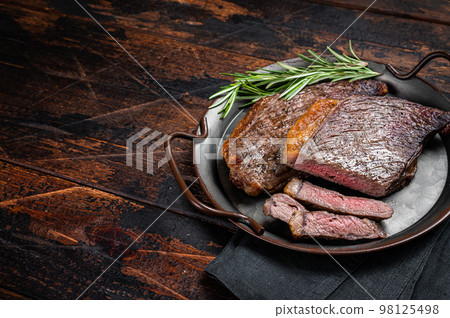 Grilled picanha or top sirloin beef steak with rosemary in steel tray. Wooden background. Top view. Copy space 98125498