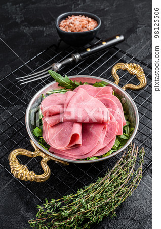 Thin slices of ham in a skillet with arugula salad. Black background. Top view Thin slices of ham in a skillet with arugula salad. Black background. Top view 98125506