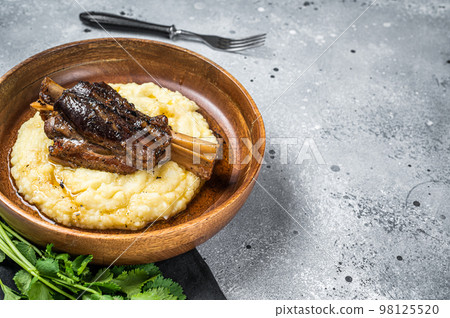Braised lamb shank on the mashed potato in a plate. Gray background. Top view. Copy space 98125520