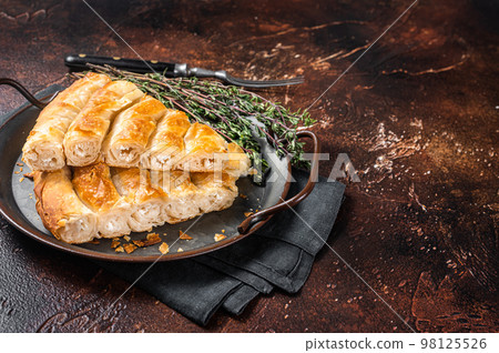 Slices of baked Round Borek cheese pie in kitchen tray with herbs. Dark background. Top view. Copy space Slices of baked Round Borek cheese pie in kitchen tray with herbs. Dark background. Top view. Copy space 98125526