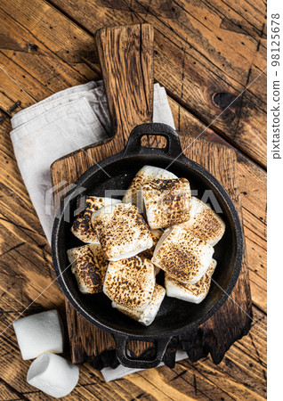 Toasted Marshmallow on open campfire in a skillet. Wooden background. Top view Toasted Marshmallow on open campfire in a skillet. Wooden background. Top view 98125678