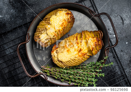 Baked hasselback potatoes with cheese, garlic, thyme and rosemary. Black background. Top view 98125698