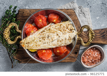 Roasted Haddock fish fillet in skillet with tomato and potato. Gray background. Top view Roasted Haddock fish fillet in skillet with tomato and potato. Gray background. Top view 98125771