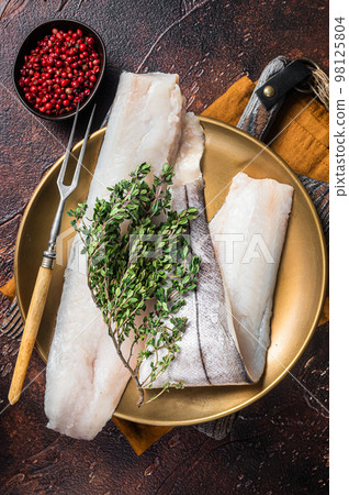 Whitefish fillet, raw Haddock fish on plate with rosemary and thyme. Dark background. Top view 98125804