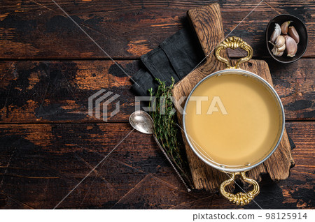 Clear broth stock without meat in cooking skillet. Wooden background. Top view. Copy space 98125914
