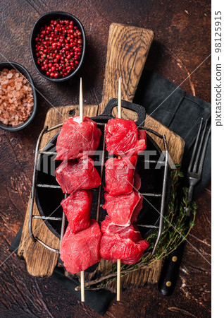 Lamb shish kebab, Raw meat Skewers with herbs on grill. Dark background. Top view Lamb shish kebab, Raw meat Skewers with herbs on grill. Dark background. Top view 98125915