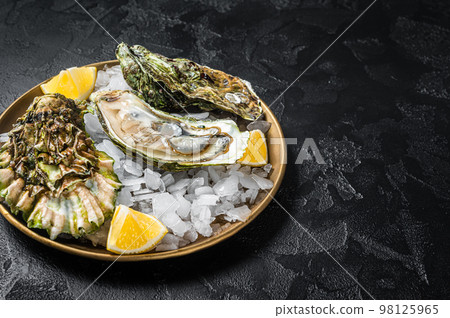 Fresh oysters with lemon on ice. Dark background. Top view. Copy space 98125965