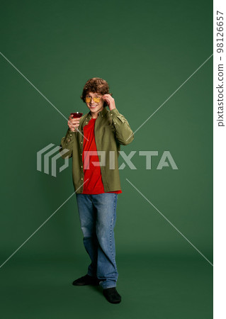 Portrait of Caucasian young handsome man in casual style clothes standing with wine glass against green background. Love, St. Valentine's day, greetings concept 98126657