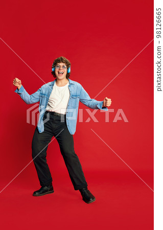 Portrait of young excited man, student in headphones dancing isolated on red background. Concept of positive emotions, happiness, youth culture. 98126665