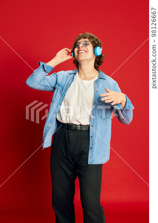 Portrait of young excited man, student in headphones dancing isolated on red background. Concept of positive emotions, happiness, youth culture. 98126667