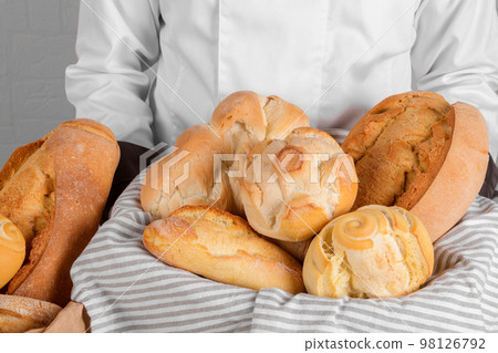 Baker holding a fresh italian wheat breads in the basket on white wall background Baker holding a fresh italian wheat breads in the basket on white wall background 98126792