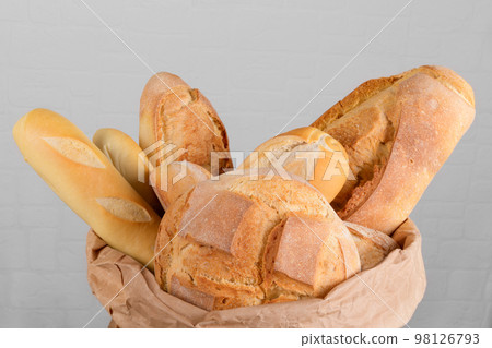 Fresh italian wheat breads in the basket and in the paper bag on the table on white wall background, close up 98126793