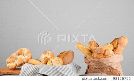 Fresh italian wheat breads in the basket and in the paper bag on the table on white wall background, banner 98126795