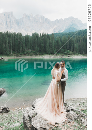 Wedding couple on the nature is hugging each other near a beautiful lake in the mountains.. Beautiful model girl in white dress. Man in suit 98126796