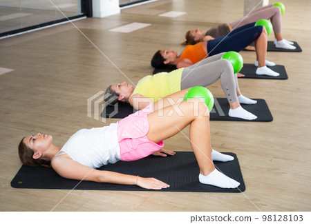 Women practicing pilates with balls at group class in yoga studio Women practicing pilates with balls at group class in yoga studio 98128103