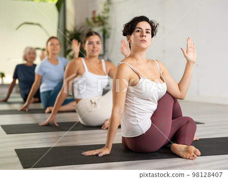 Young concentration girl maintaining mental and physical health attending group yoga class at studio, practicing twisting poses 98128407