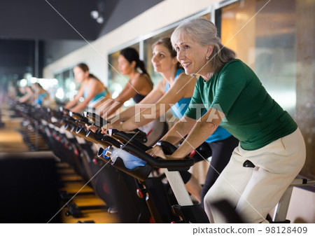 Mature woman taking cycling class at gym Mature woman taking cycling class at gym 98128409