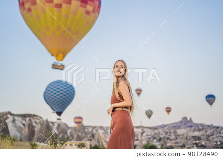 Tourist woman looking at hot air balloons in Cappadocia, Turkey. Happy Travel in Turkey concept. Woman on a mountain top enjoying wonderful view 98128490