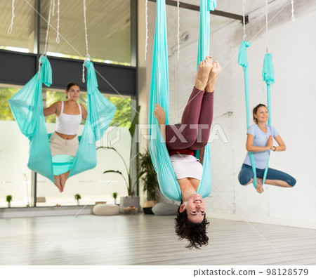 Group of women hang upside down in a hammock. Fly yoga class in gym. Fit and wellness lifestyle 98128579