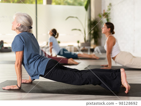 Mature woman performing Bhujangasana or Cobra pose during yoga class with female group in fitness studio 98128692