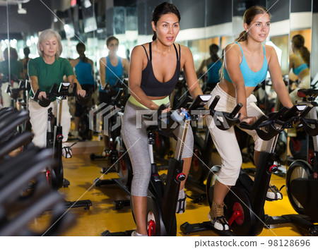 Women training on stationary bikes at gym Women training on stationary bikes at gym 98128696