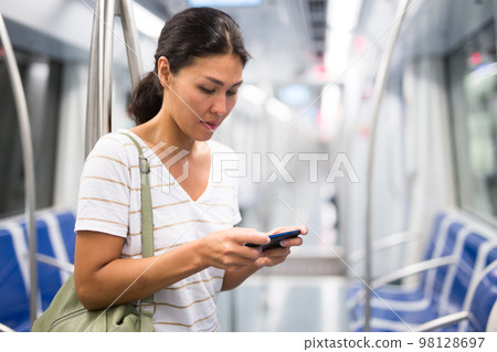 Woman with smartphone standing in metropolitan train 98128697