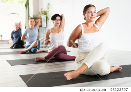 Young woman maintaining mental and physical health attending group yoga class at studio, practicing twisting poses 98128707