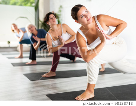 Calm young woman practicing Revolved Side Angle Pose Parivrtta Parsvakonasana, balancing posture of Hatha yoga during group workout in studio Calm young woman practicing Revolved Side Angle Pose Parivrtta Parsvakonasana, balancing posture of Hatha yoga during group workout in studio 98128718