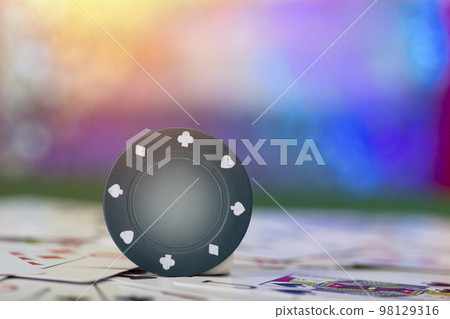 A green chip balances on a table with playing cards on it 98129316