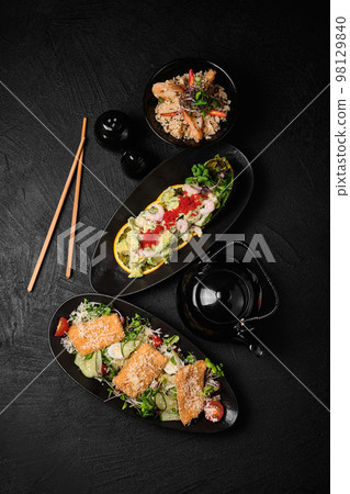 Caesar salad, avocado salad, rice and chopsticks in Japanese stile on a black concrete background. 98129840