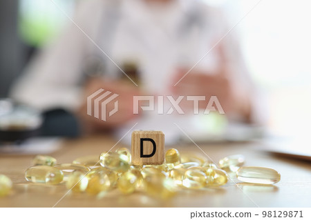 Dietician doctor and pile of vitamin D capsules with D symbol on wooden cube. 98129871