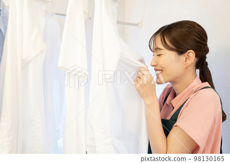 A woman who smells a shirt that is dried in the bathroom and smiles A woman who smells a shirt that is dried in the bathroom and smiles 98130165