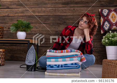 After finishing ironing the towels, the girl gets dreamy and looks up. 98130176